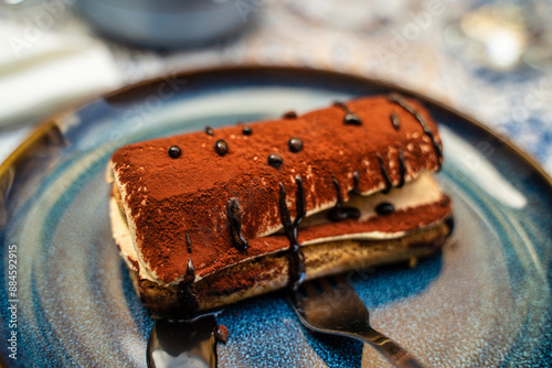 Obraz na płótnie Delicious Tiramisu Dessert Served On Blue Plate with Chocolate Drizzle w salonie