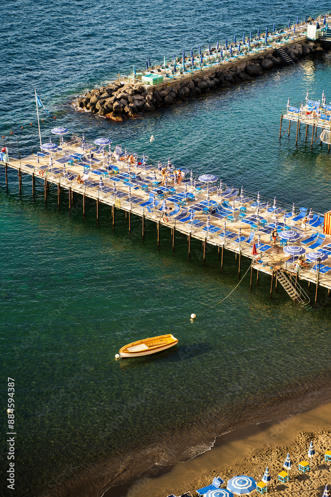 Sorrento, Italy - June 20, 2024: Beautiful coastal view of a marina in Sorrento, Italy with boats, piers, and vibrant striped beach huts against water body
