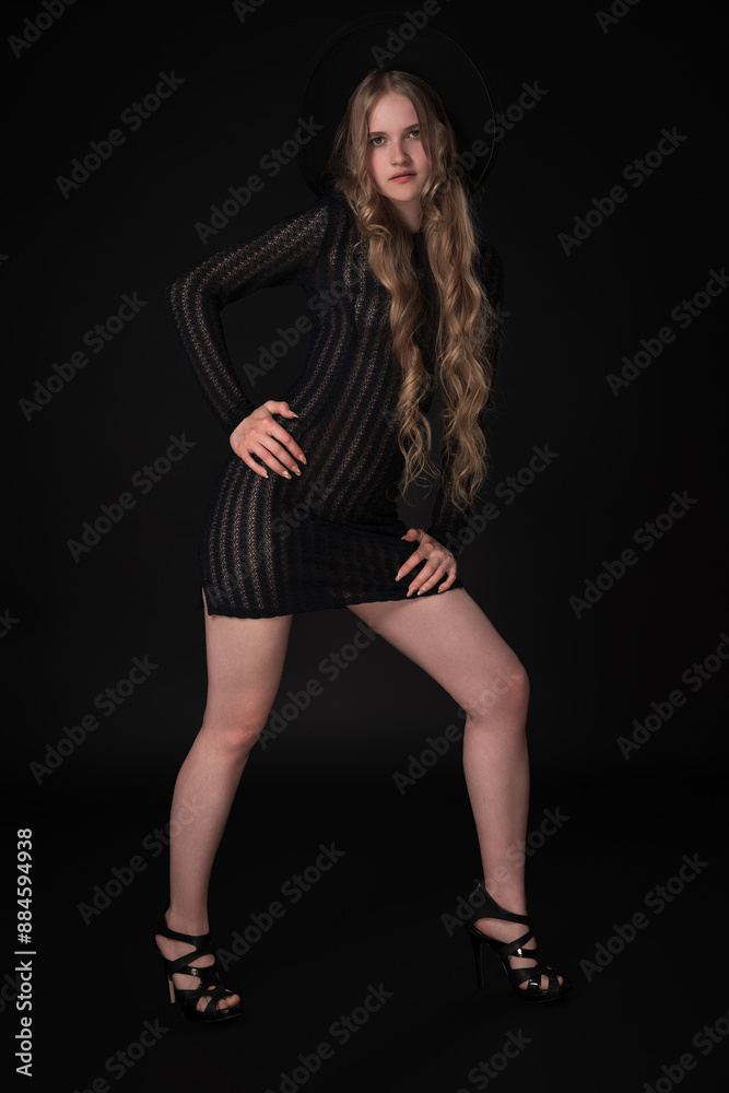 Full length portrait portrait of blonde model exudes confidence as she strikes pose on black background, gazing at camera. Fashionista is rocking chic black dress, complete with wide-brimmed felt hat Full length portrait portrait of blonde model exudes confidence as she strikes pose on black background, gazing at camera. Fashionista is rocking chic black dress, complete with wide-brimmed felt hat