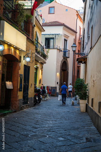 Sorrento, Italy - June 20, 2024: People walking on a narrow street during an evening between a colorful building of residence houses and commercial shops