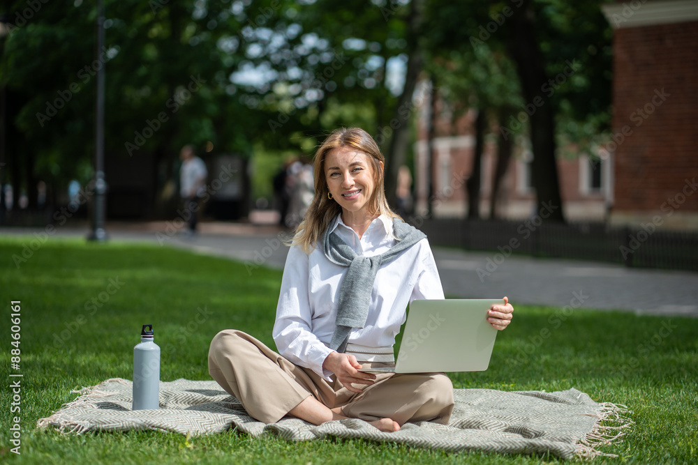 Obraz premium Smiling businesslike woman working remotely online using portable computer. Cheerful female relaxing resting outside outdoors in public place in nature. Joyful woman employee busy with job tasks.