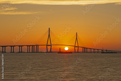 Silhouette and sunset view of two barge ships moored on the sea against Incheon Bridge with piers and pillars near Yeonsu-gu, Incheon, South Korea 