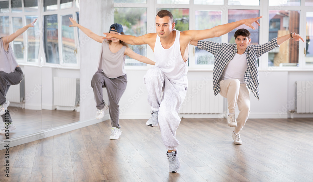 Fototapeta premium Active young guy practicing hip-hop reject step in training hall during dancing classes