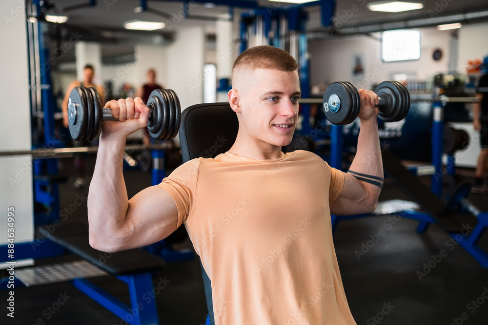 Young bodybuilder lifts dumbbells while sitting on a bench in a gym Young bodybuilder lifts dumbbells while sitting on a bench in a gym