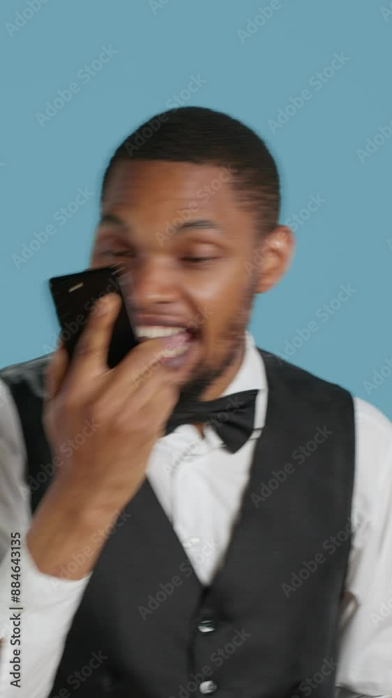 Vertical Video Hotel porter in tuxedo making reservations on phone call in studio, discussing with future guests about lodging and amenities. Doorkeeper hotelier on telephone line. Camera A. Vertical Video Hotel porter in tuxedo making reservations on phone call in studio, discussing with future guests about lodging and amenities. Doorkeeper hotelier on telephone line. Camera A.