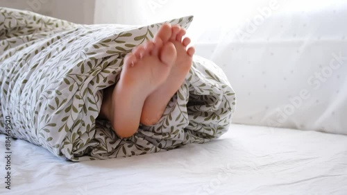 Rolled person. A child wrapped in a blanket with sticking out feet and head lies on the bed in the bedroom. Psychology discomfort. Bad children jokes. Teasing through tickling. Bullying by tickle