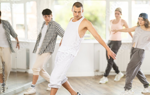 Active young guy practicing basic hip-hop steps in training hall during dancing classes