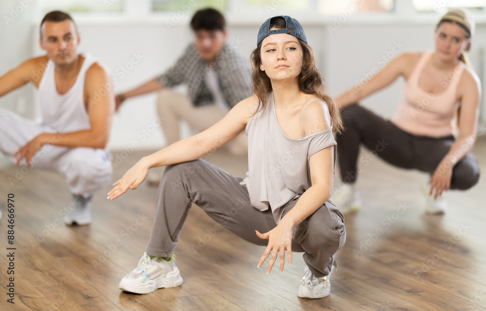 Obraz premium Dynamic young woman training breakdance sitting pose in dancehall during workout session