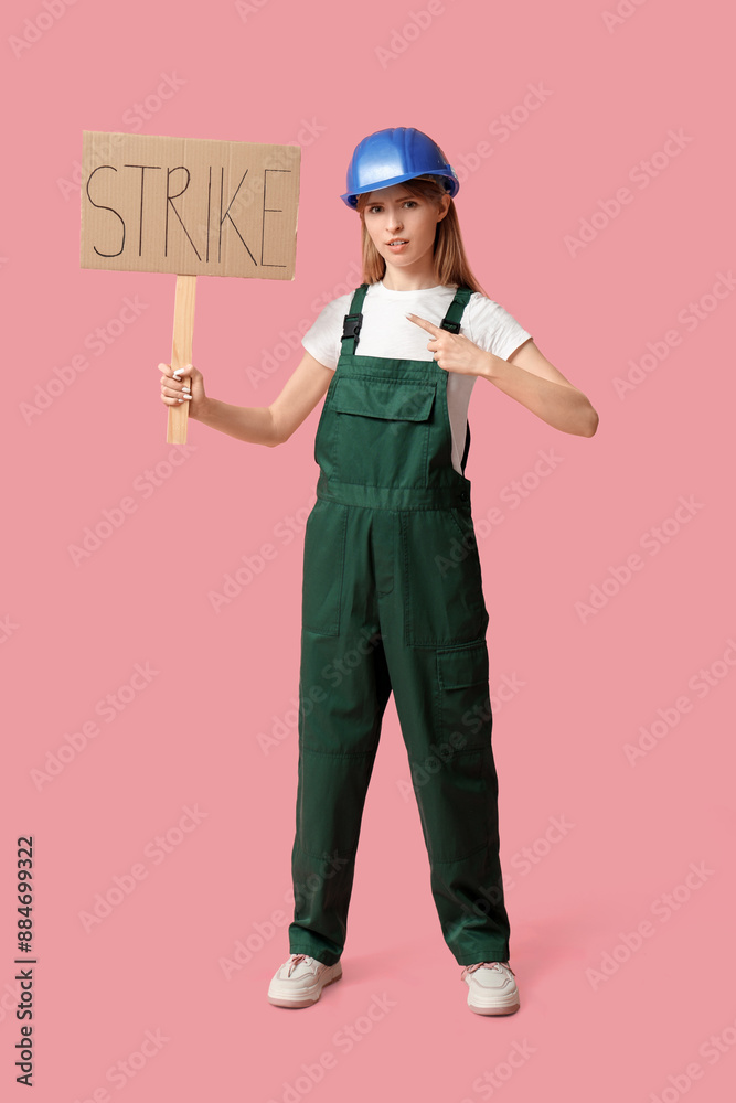 Protesting female construction worker holding placard with text STRIKE on pink background Protesting female construction worker holding placard with text STRIKE on pink background