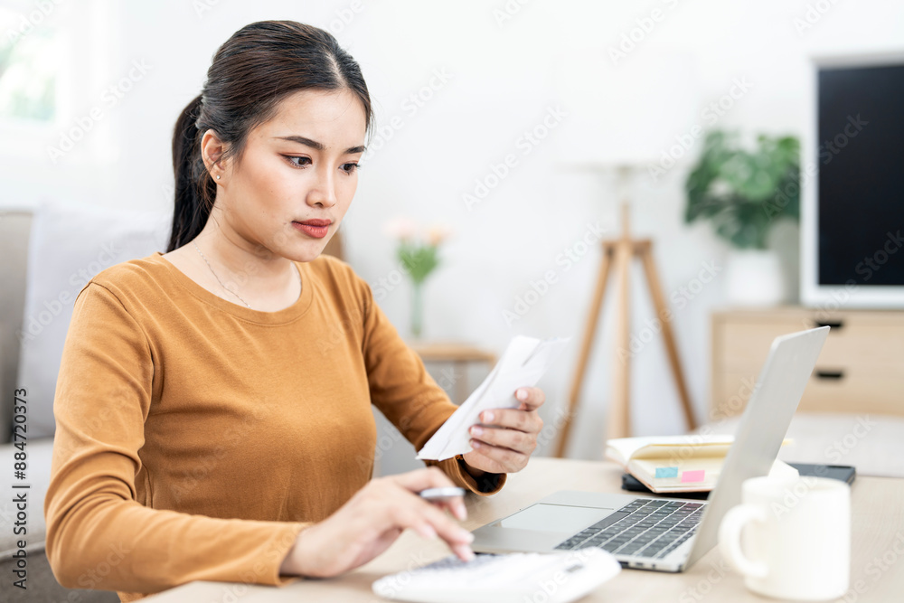 Woman work on laptop at home checking bills for payments, holding receipts, getting upset about overspending Woman work on laptop at home checking bills for payments, holding receipts, getting upset about overspending