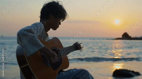 夕焼けの海でアコースティックギターを弾くアジア人男性