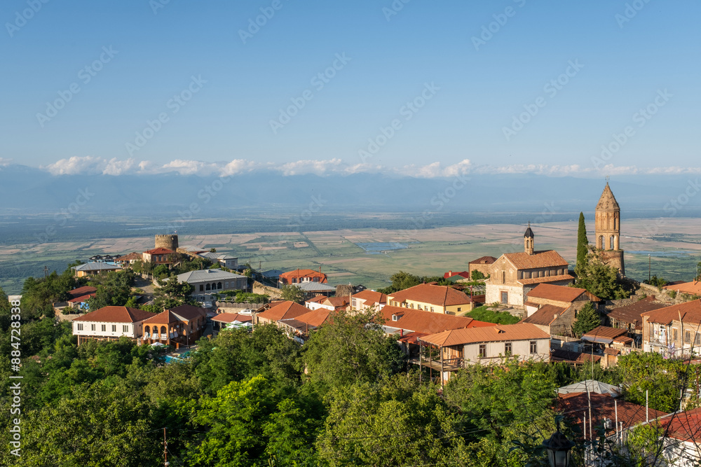 A charming European town with red-roofed buildings, a church with a tall steeple, rolling hills, and majestic mountains in the background A charming European town with red-roofed buildings, a church with a tall steeple, rolling hills, and majestic mountains in the background