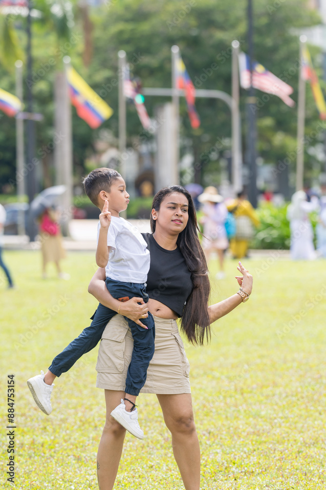 Obraz premium A thirty-something Indian Malaysian mother joyfully playing on the expansive lawn at Merdeka Square in Kuala Lumpur, Malaysia, while holding her seven-year-old son.