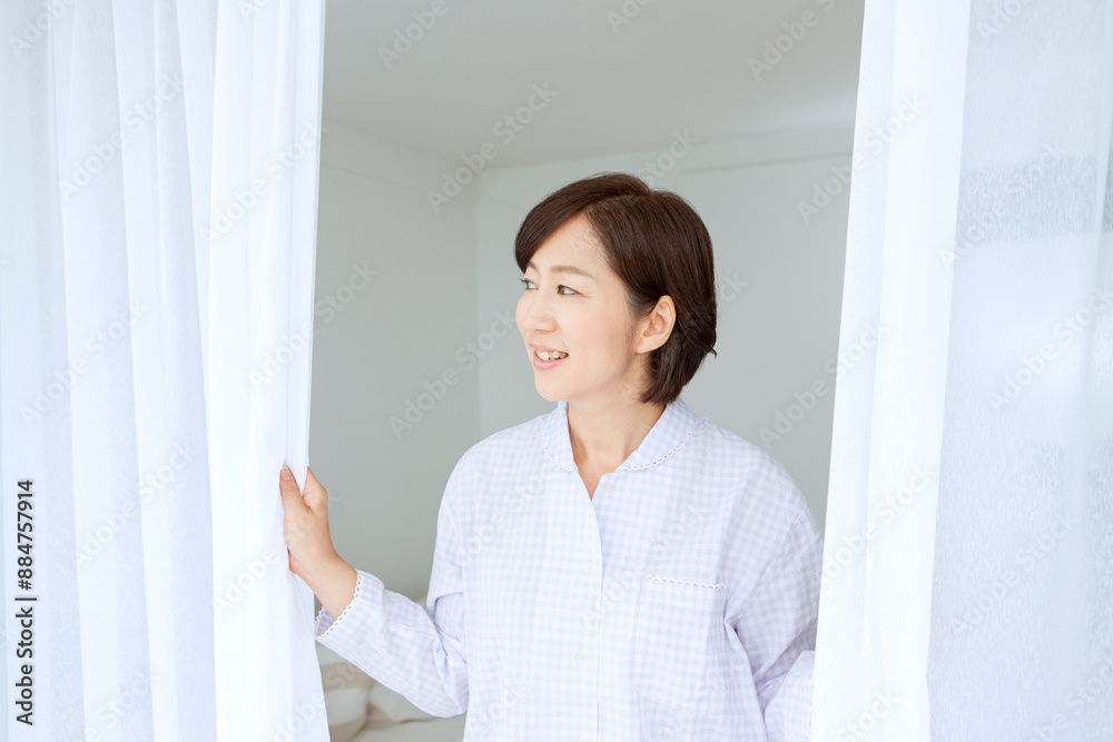 カーテンを開けるパジャマ姿の中年女性