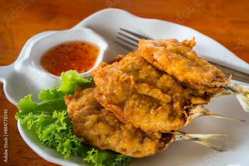 Fried mackerel fish with Crispy fried dough that eat with sauce . Food in the white plate on the wooden table at the seafood restaurant. 