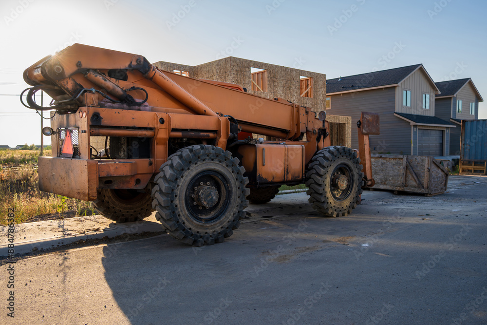 Orange telehandler equipment in front of new residential duplex homes under construction. Orange telehandler equipment in front of new residential duplex homes under construction.