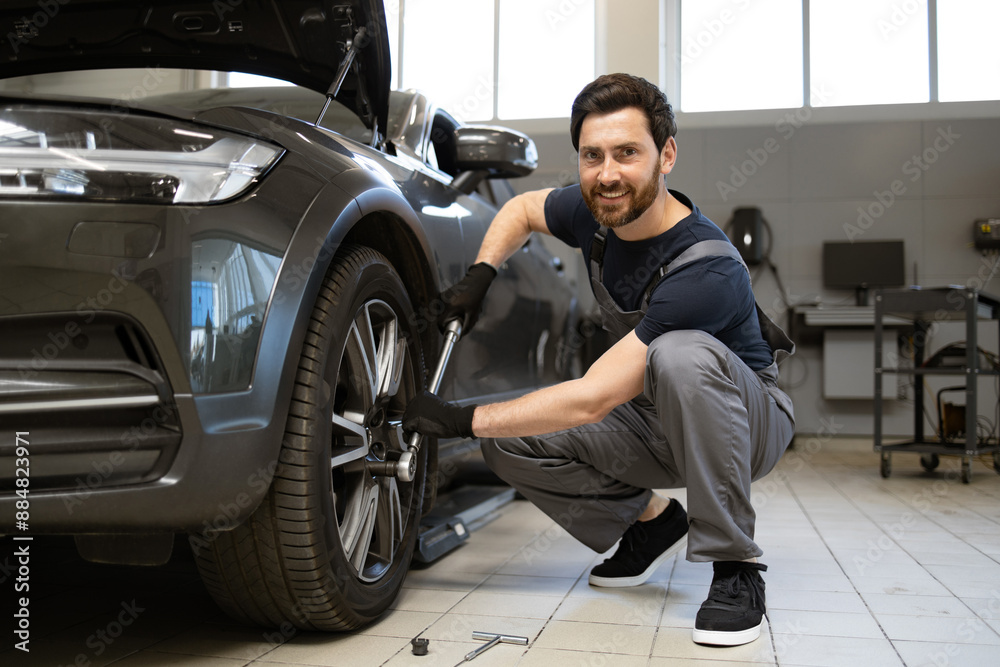 Mechanic in auto repair shop working on car wheel, using wrench. Professional mechanic delivering car maintenance service with smile. Modern workshop environment with car repair tools. Mechanic in auto repair shop working on car wheel, using wrench. Professional mechanic delivering car maintenance service with smile. Modern workshop environment with car repair tools.