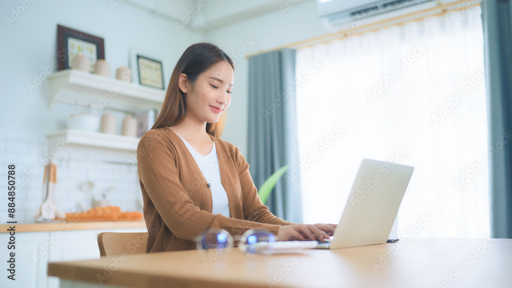 Fototapeta premium Beautiful young Asian woman working with laptop computer in home kitchen. Work at home