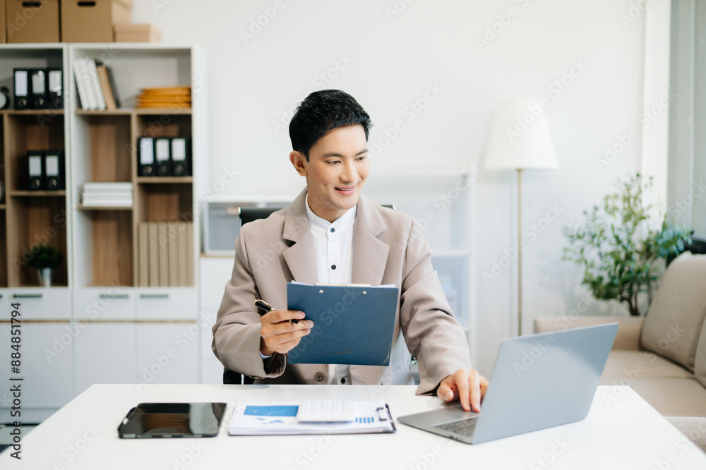 Young Asian man using laptop and tablet while sitting at her working place. Young Asian man using laptop and tablet while sitting at her working place.
