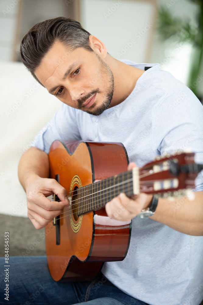 Obraz premium pretty young man playing guitar while sitting on sofa