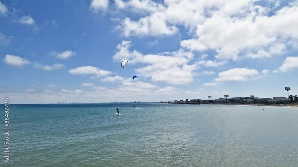 General shot of people kitesurfing with hydrofoil on a blue sea beach on a sunny day with the city in the background General shot of people kitesurfing with hydrofoil on a blue sea beach on a sunny day with the city in the background