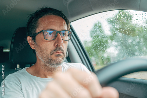 Driving a car with poor eyesight, portrait of mature adult male driver with eyeglasses holding a vehicle steering wheel