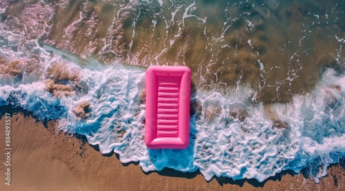 A pink rectangular air mattress floating on the beach in a drone shot top view. Ocean waves hit the shore in a cinematic and realistic style of photography at high resolution