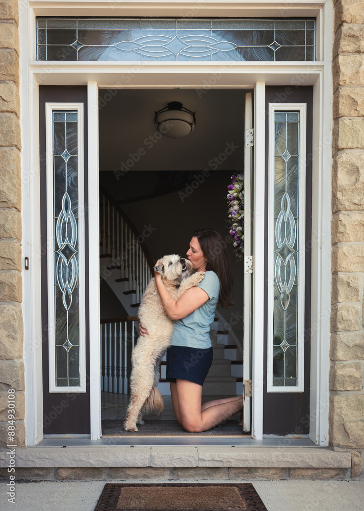 Woman hugging furry dog in front door after coming home. Woman hugging furry dog in front door after coming home.