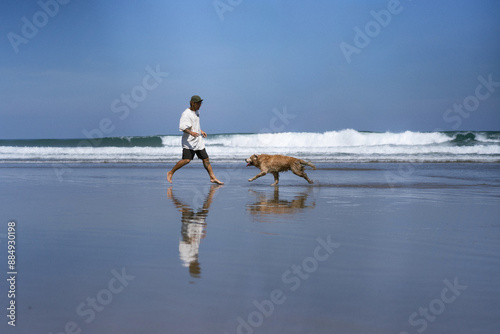 Man plays on the beach with a dog, they run around and fool around. photo