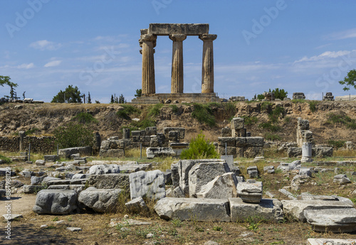 Corinth, Peloponnesus, Greece - August 10, 2023: Summer view of stone ruins against pillars on the hill at Temple of Apollo
 photo