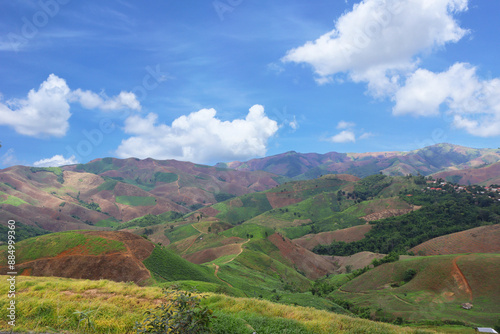 Expansive highland view showcasing vibrant green valleys and deforestation under a bright blue sky, symbolizing nature's beauty