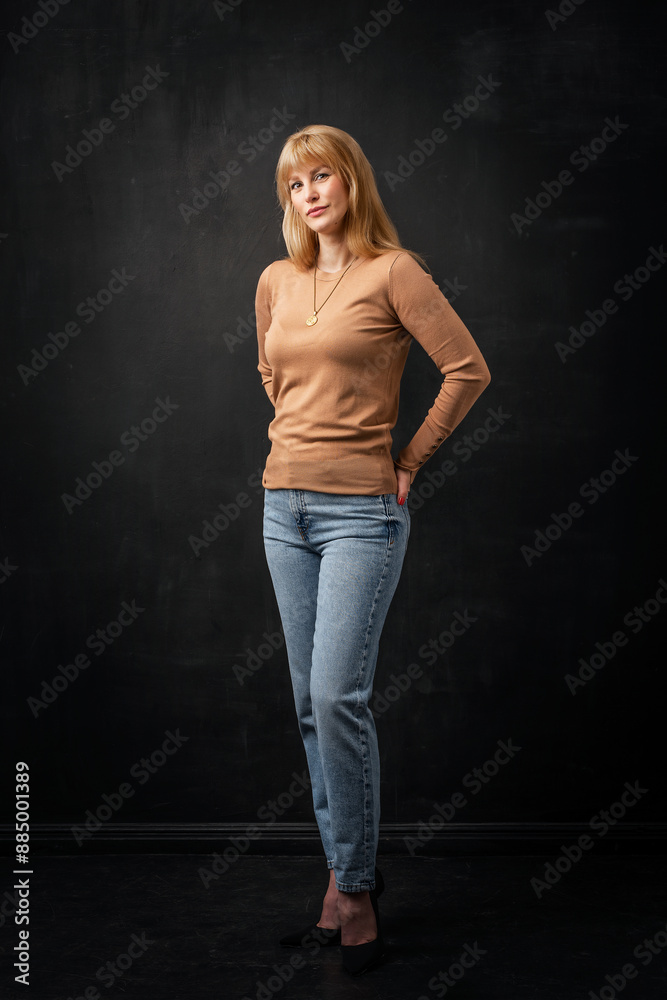 Full length studio portrait of a blond haired woman standing against isolated dark background Full length studio portrait of a blond haired woman standing against isolated dark background