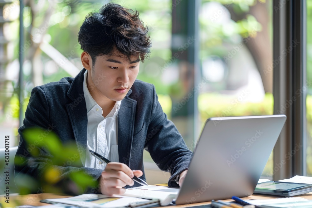 Young Asian business man working at office with laptop, tablet and taking notes on the paper. Young Asian business man working at office with laptop, tablet and taking notes on the paper.