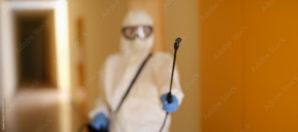 Person in protective suit holding disinfection equipment in hand. Respirator disinfects of apartment with chemical agent, sanitation worker cleans room from coronavirus Person in protective suit holding disinfection equipment in hand. Respirator disinfects of apartment with chemical agent, sanitation worker cleans room from coronavirus