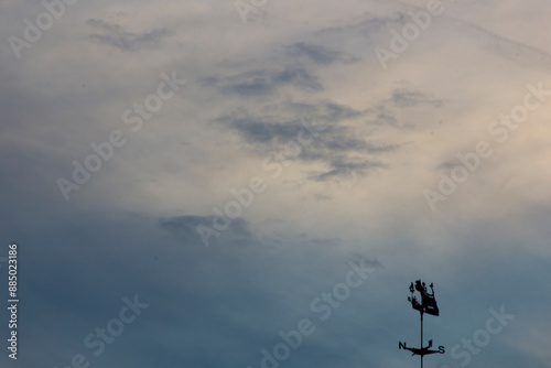 Silhouette of wind vane against the sky with clouds.