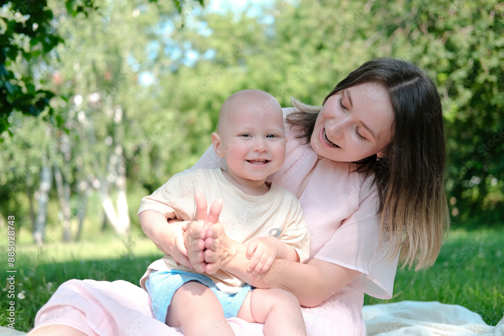 Happy mother plays with her child in park in summer. Parent and child spend time together in sunlight. Environmentally sustainable lifestyle. Positive emotions. Hugs and kisses. Selective focus. Happy mother plays with her child in park in summer. Parent and child spend time together in sunlight. Environmentally sustainable lifestyle. Positive emotions. Hugs and kisses. Selective focus.