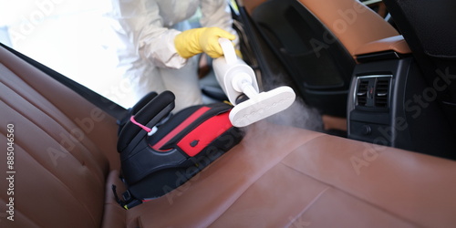 Φωτογραφία Close-up of worker in uniform cleanse car interior using steam cleaner with spray disinfectant