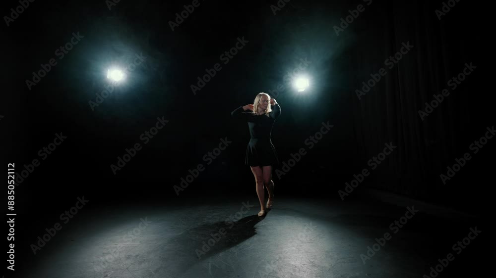 Beautiful woman rehearsing modern choreography in dark dancehall, slow motion. Female dancer moving slowly on stage with bright soffits, graceful lady in short black dress, contemporary dance show Beautiful woman rehearsing modern choreography in dark dancehall, slow motion. Female dancer moving slowly on stage with bright soffits, graceful lady in short black dress, contemporary dance show