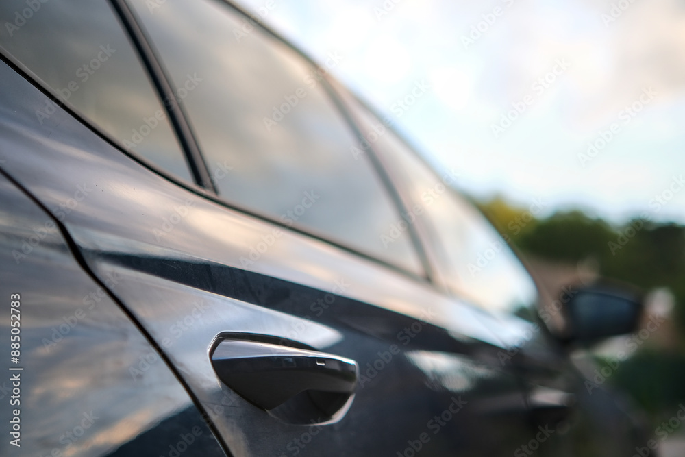 Fototapeta premium Blurred side view of a car parked in a driveway, focusing on the rear door handle, with perspective effect.