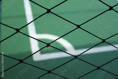 a close-up of a black chain-link fence with a blurred background featuring a green sports court with white boundary lines.