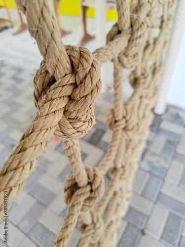 a close-up of a thick, twisted rope with a knot in the center. The focus is on the knot and part of the rope, with other strands extending into the background which is blurred. 