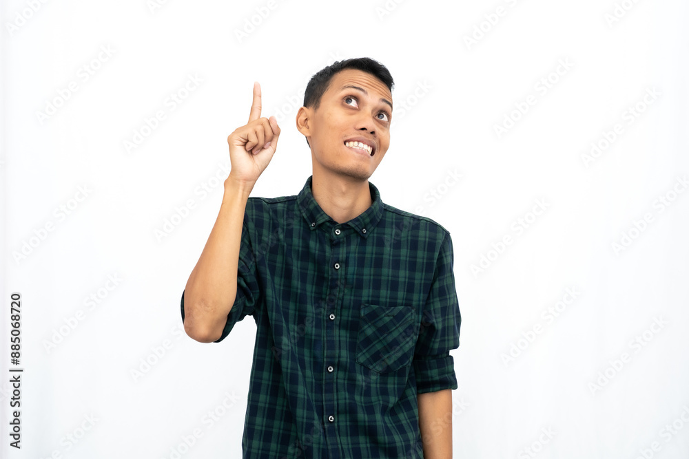 Asian man wearing a green checkered casual shirt pointing towards an empty space for advertising. Isolated white background. Asian man wearing a green checkered casual shirt pointing towards an empty space for advertising. Isolated white background.
