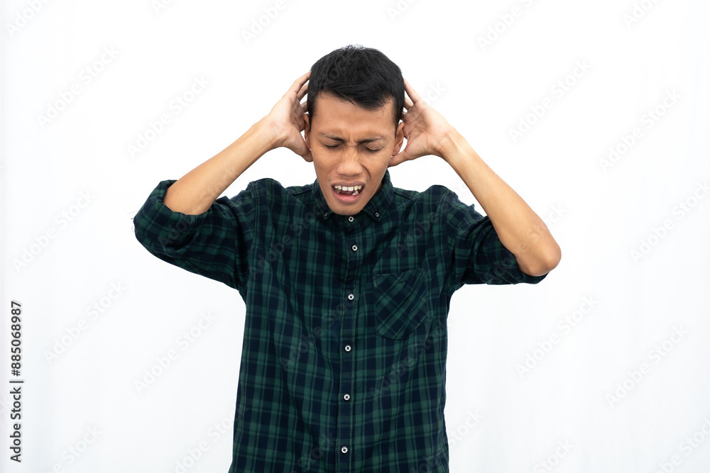 Asian man wearing a green checkered casual shirt holding his head experiencing high levels of stress and screaming. Isolated white background. Asian man wearing a green checkered casual shirt holding his head experiencing high levels of stress and screaming. Isolated white background.