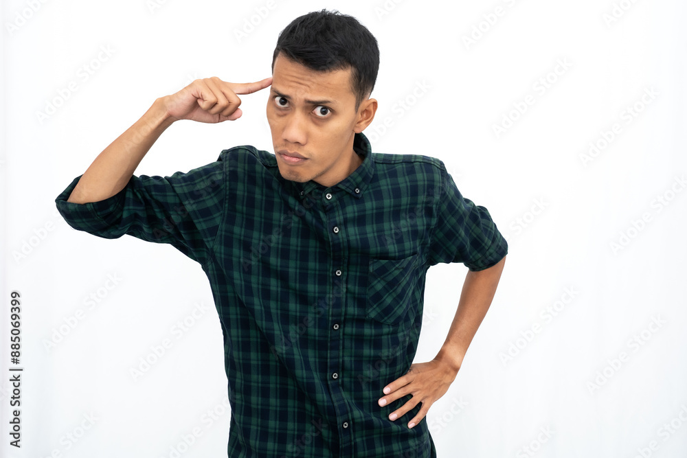 An Asian man wearing a casual green checkered shirt gave off an angry expression while pointing his finger at his brain to tell it to think. Isolated white background. An Asian man wearing a casual green checkered shirt gave off an angry expression while pointing his finger at his brain to tell it to think. Isolated white background.