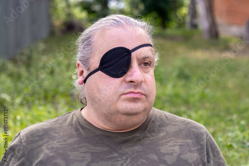 Portrait of a blind, visually impaired man with a black medical patch on his eye in the park