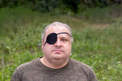 Portrait of a blind, visually impaired man with a black medical patch on his eye in the park