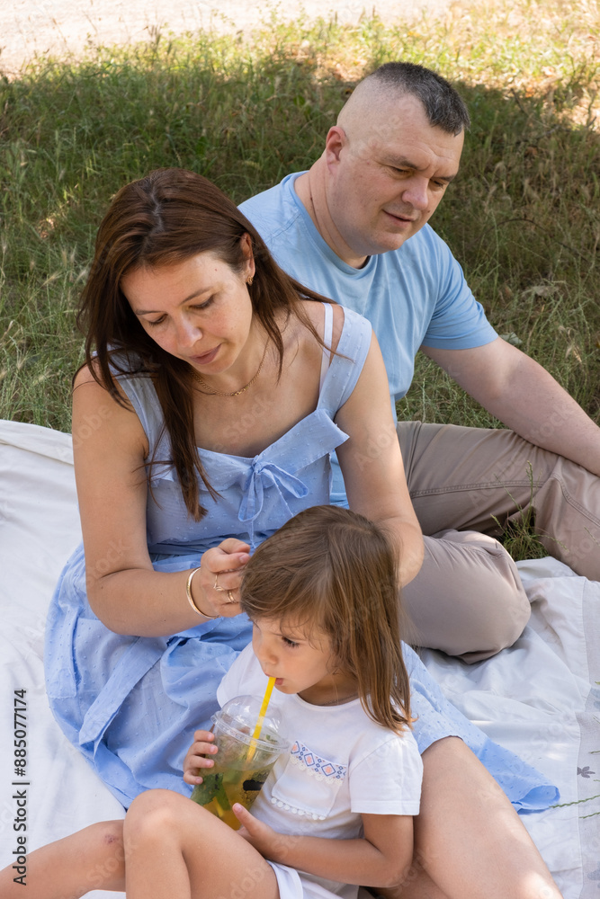 Fototapeta premium Mom, dad and daughter having fun on a picnic. Family vacation in nature