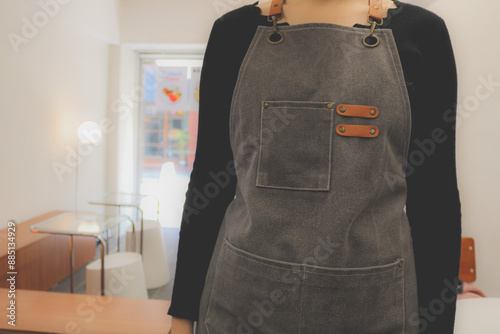 Close-up of a waitress wearing a denim apron in a cozy cafe. Detail of a barista uniform with the cafeteria hall in the background.