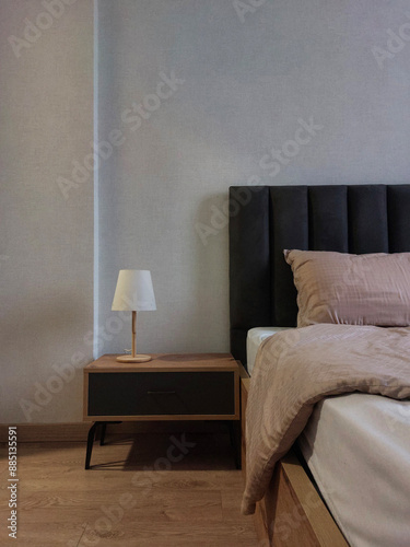 Cozy and minimalist bedroom corner with a bed and with a table lamp on a wooden nightstand