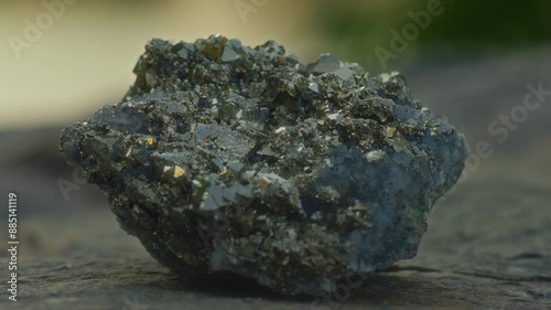 Close-up, large pyrite crystal lying on a rock with lake in the background